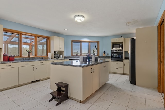 kitchen with light tile patterned flooring, dark stone countertops, appliances with stainless steel finishes, a kitchen island, and cream cabinets