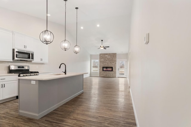 kitchen with hanging light fixtures, stainless steel appliances, ceiling fan with notable chandelier, dark wood-type flooring, and a fireplace