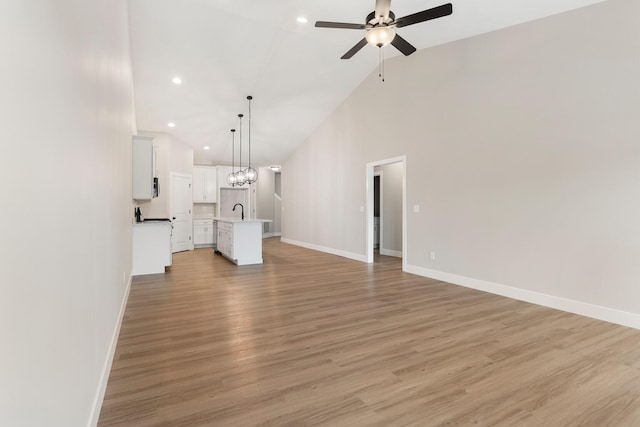 unfurnished living room with high vaulted ceiling, ceiling fan with notable chandelier, sink, and light hardwood / wood-style floors