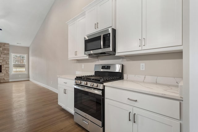 kitchen featuring light stone counters, lofted ceiling, white cabinets, stainless steel appliances, and wood-type flooring