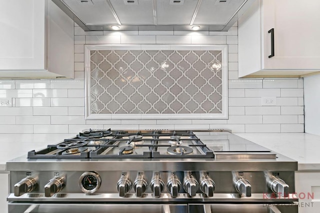 kitchen featuring tasteful backsplash, gas range oven, white cabinets, and light stone countertops