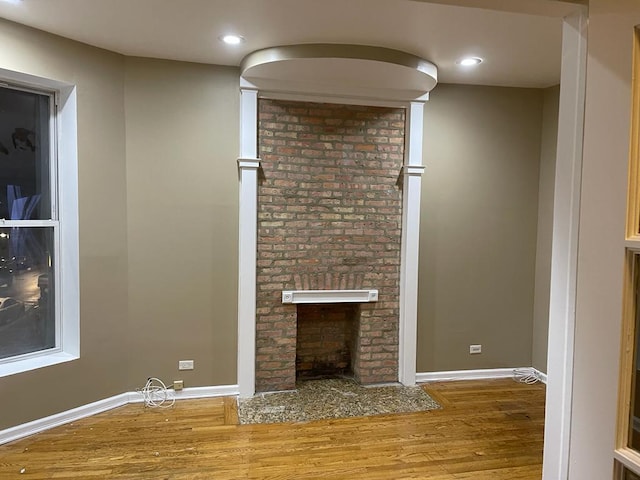 unfurnished living room featuring hardwood / wood-style flooring and a brick fireplace