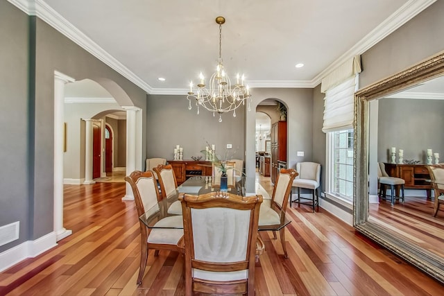 dining space featuring wood-type flooring, ornate columns, an inviting chandelier, and crown molding