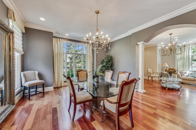 dining room with a notable chandelier, ornamental molding, wood-type flooring, and ornate columns