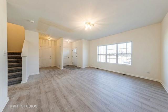 unfurnished living room with visible vents, stairs, baseboards, and wood finished floors