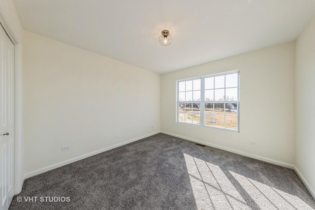 unfurnished room featuring dark colored carpet, visible vents, and baseboards