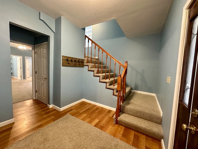 stairs featuring a textured ceiling and light hardwood / wood-style floors