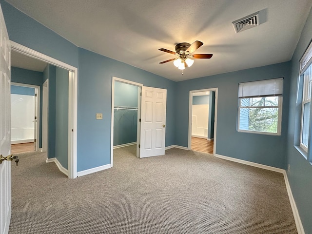 unfurnished bedroom with a closet, a spacious closet, light colored carpet, and ceiling fan