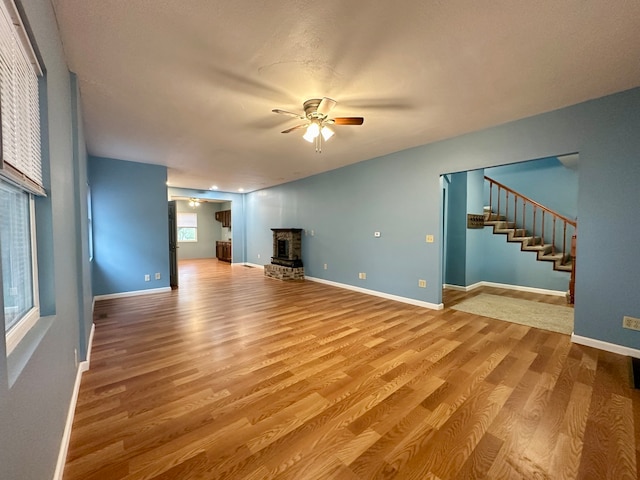 unfurnished living room featuring a wealth of natural light, ceiling fan, light wood-type flooring, and a fireplace