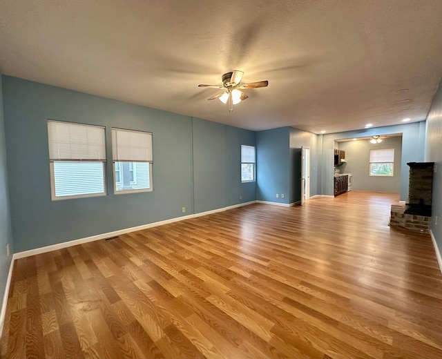 unfurnished living room with a stone fireplace, ceiling fan, and light hardwood / wood-style flooring