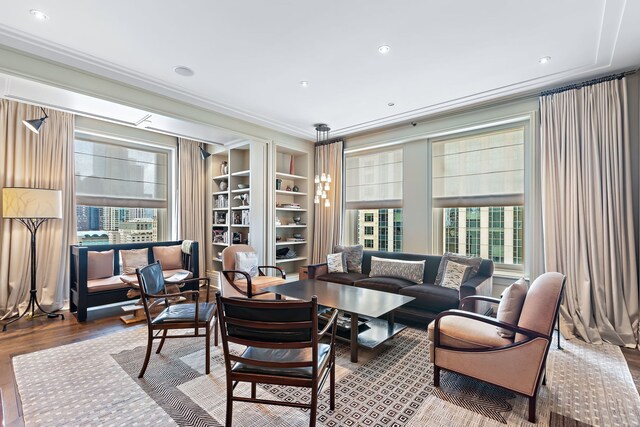 living room featuring built in shelves, crown molding, and wood finished floors