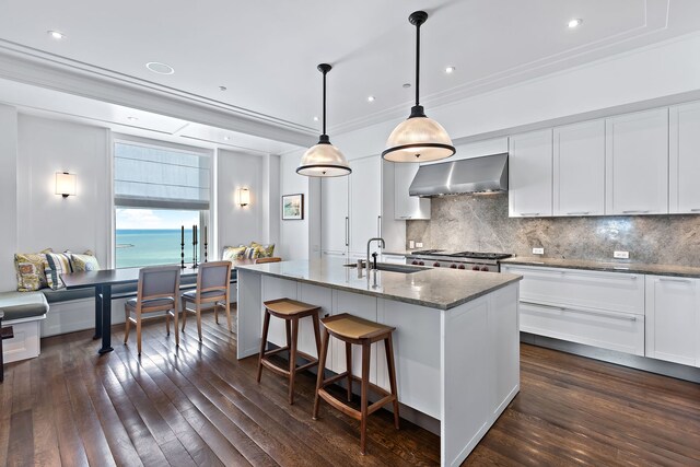 kitchen featuring wall chimney exhaust hood, dark wood-style flooring, a sink, and white cabinetry