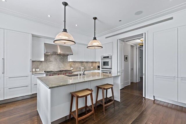 kitchen with ornamental molding, dark wood-type flooring, white cabinets, a sink, and wall chimney range hood