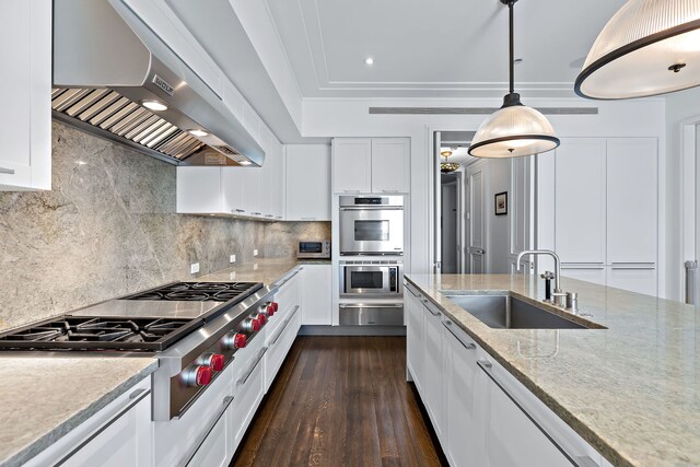 kitchen with a warming drawer, stainless steel appliances, white cabinetry, a sink, and wall chimney range hood