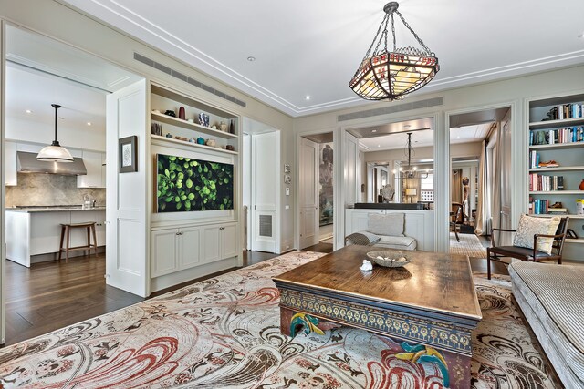 living area featuring dark wood finished floors, built in features, and an inviting chandelier