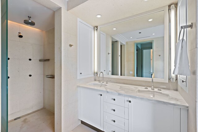 full bathroom featuring a tile shower, a sink, tile walls, and double vanity