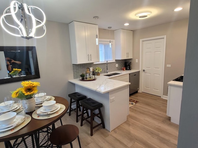 kitchen featuring pendant lighting, sink, dishwasher, white cabinets, and kitchen peninsula