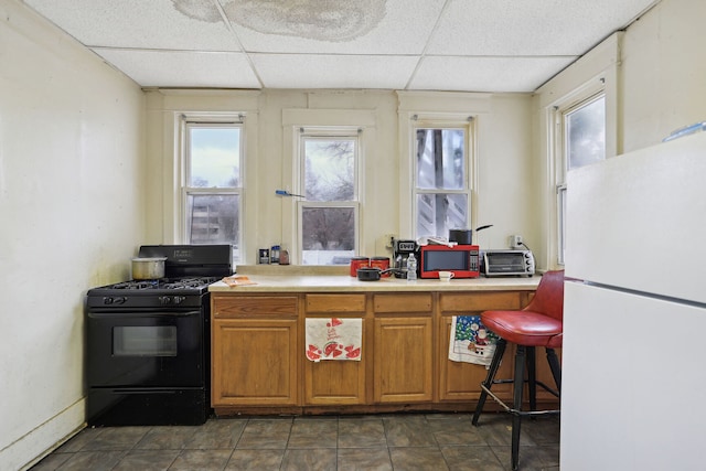 kitchen with a wealth of natural light, a paneled ceiling, black gas range, and white refrigerator