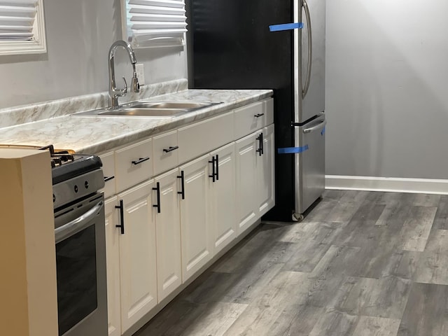 kitchen featuring appliances with stainless steel finishes, dark hardwood / wood-style flooring, light stone counters, sink, and white cabinets