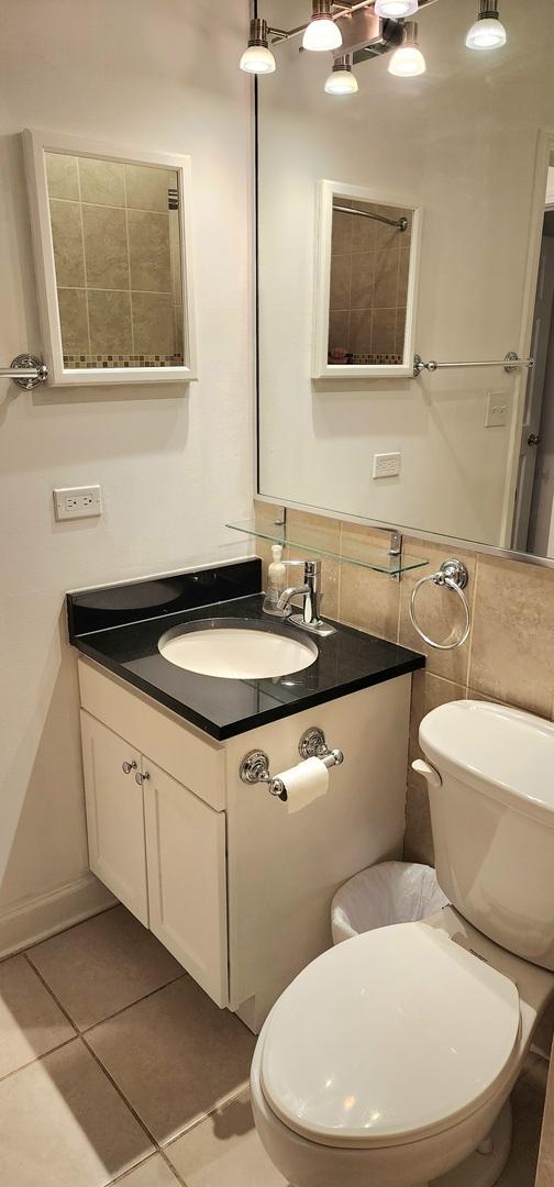 bathroom featuring tile patterned flooring, vanity, toilet, and tile walls