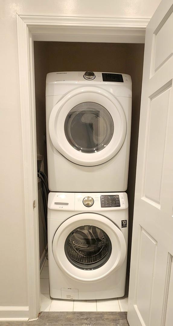 laundry room with stacked washing maching and dryer and light tile patterned flooring