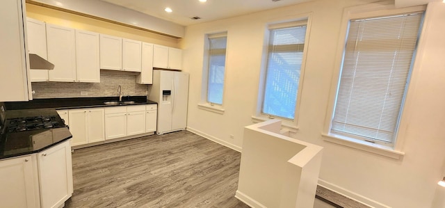 kitchen featuring sink, decorative backsplash, white fridge with ice dispenser, light hardwood / wood-style floors, and white cabinetry