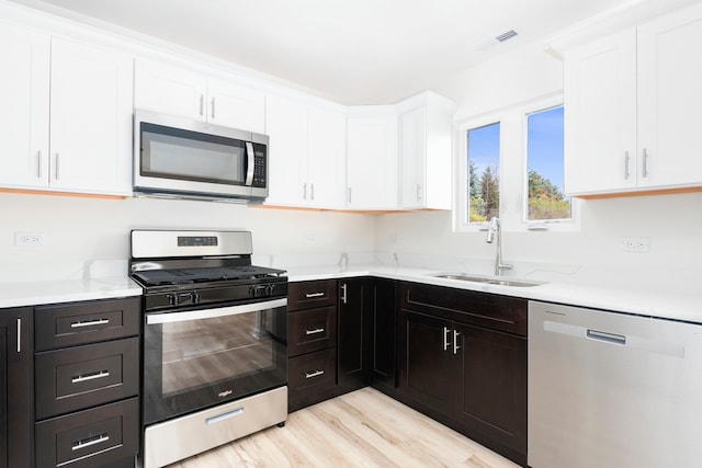 kitchen with stainless steel appliances, white cabinets, sink, light stone counters, and light wood-type flooring