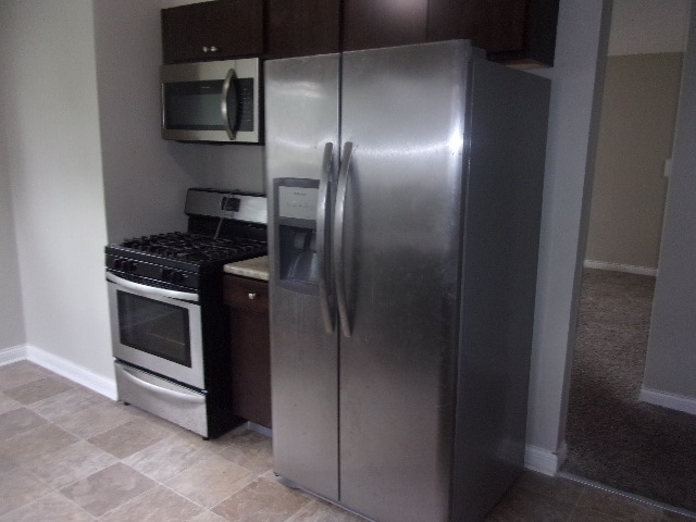 kitchen with dark brown cabinets, appliances with stainless steel finishes, and light tile floors