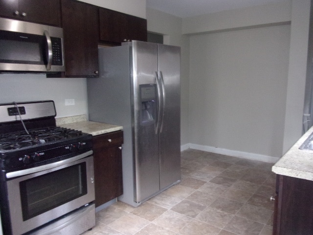 kitchen featuring light tile floors, dark brown cabinets, and stainless steel appliances