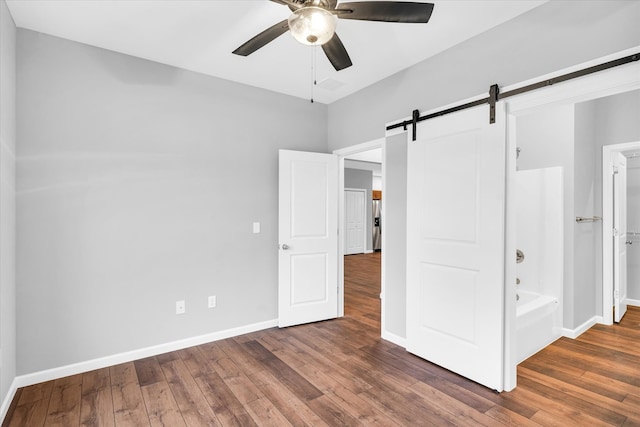 unfurnished bedroom with a barn door, dark hardwood / wood-style floors, ensuite bath, and ceiling fan