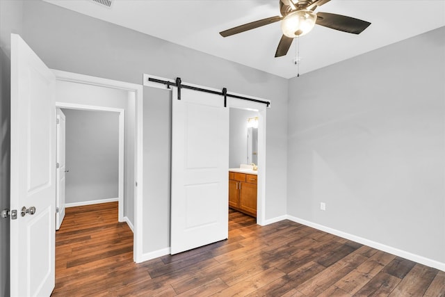 unfurnished bedroom with a barn door, ceiling fan, dark hardwood / wood-style flooring, and ensuite bath