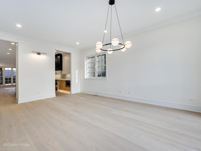 spare room with a chandelier, light hardwood / wood-style floors, and crown molding