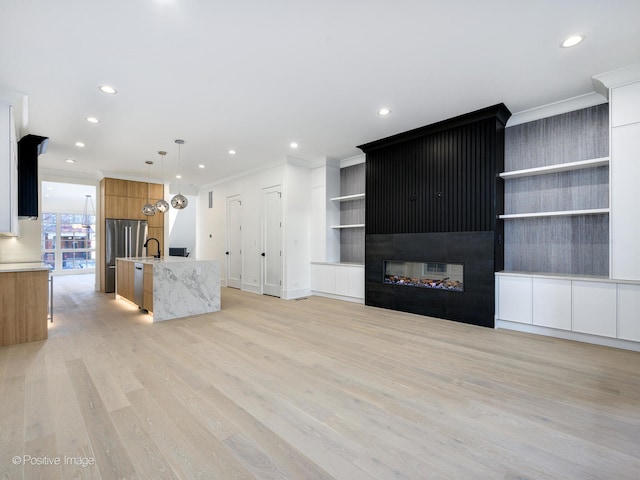 unfurnished living room featuring ornamental molding, a fireplace, sink, and light hardwood / wood-style flooring