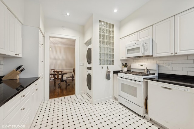 kitchen featuring stacked washer / drying machine, white appliances, decorative backsplash, and white cabinets