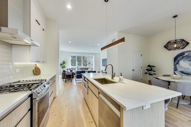 kitchen with pendant lighting, stainless steel appliances, a kitchen island with sink, and wall chimney exhaust hood