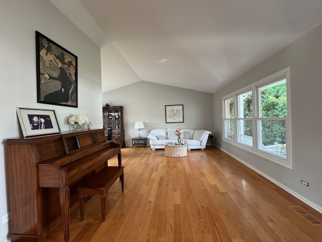 living area with visible vents, baseboards, light wood-style floors, and vaulted ceiling