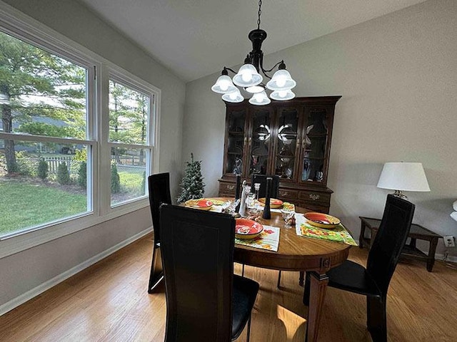 dining area featuring a chandelier, wood finished floors, baseboards, and vaulted ceiling