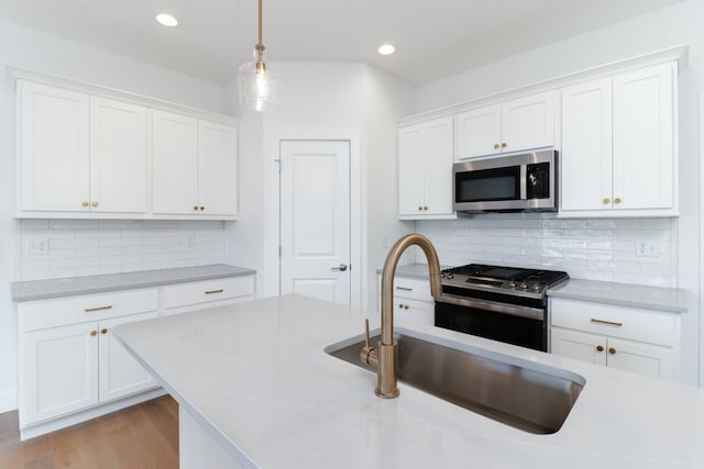 kitchen with appliances with stainless steel finishes, white cabinetry, light wood-type flooring, pendant lighting, and backsplash