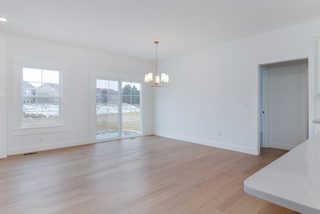 empty room with a notable chandelier, plenty of natural light, and light hardwood / wood-style flooring