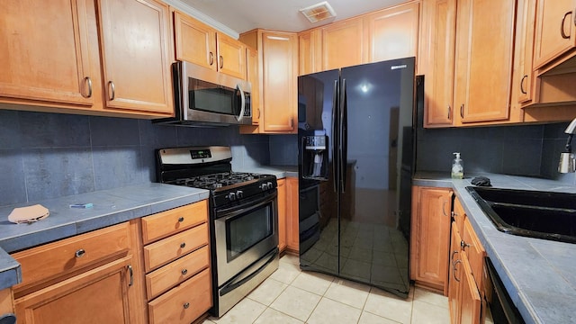 kitchen with tile counters, sink, stainless steel appliances, decorative backsplash, and light tile patterned flooring