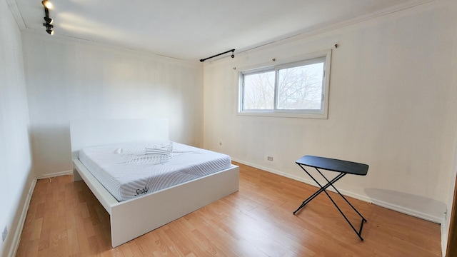 bedroom with light hardwood / wood-style floors, ornamental molding, and track lighting