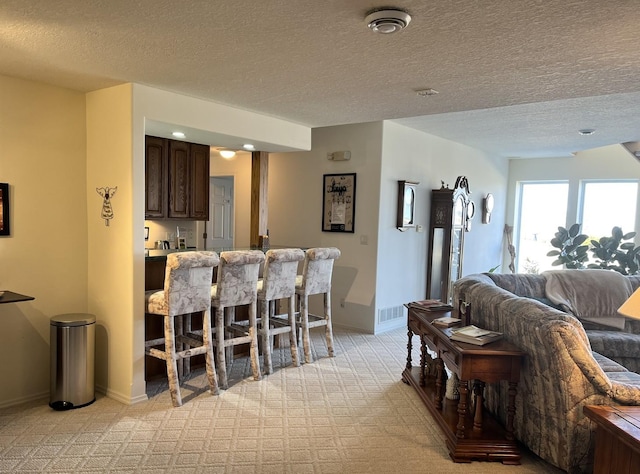 living room featuring light carpet, visible vents, baseboards, and a textured ceiling