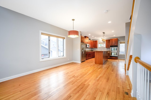 kitchen with baseboards, open floor plan, stainless steel appliances, light countertops, and light wood-style floors