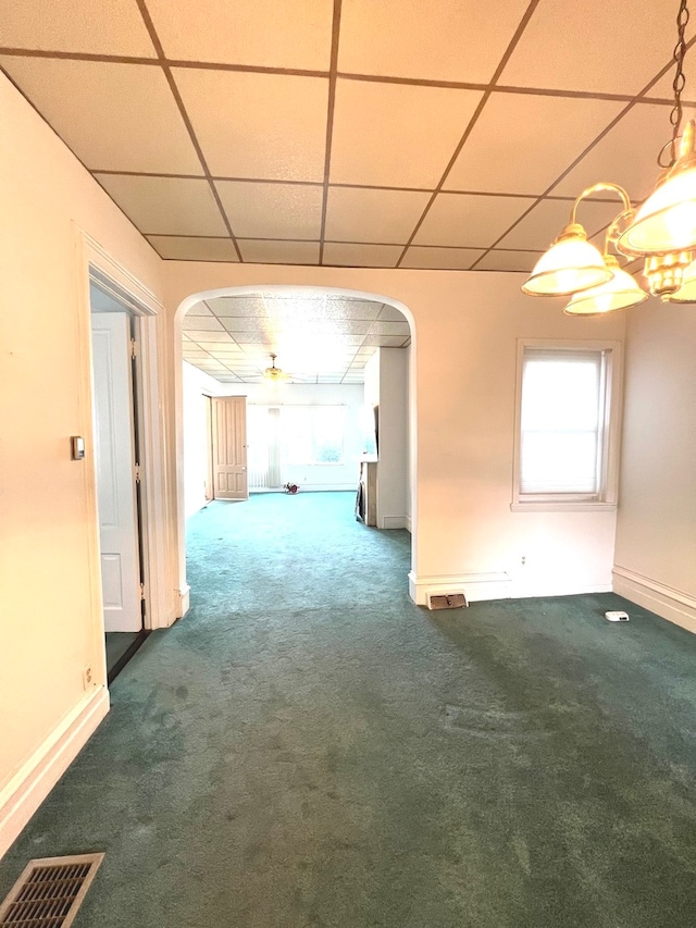 unfurnished room with a paneled ceiling, ceiling fan with notable chandelier, and dark colored carpet