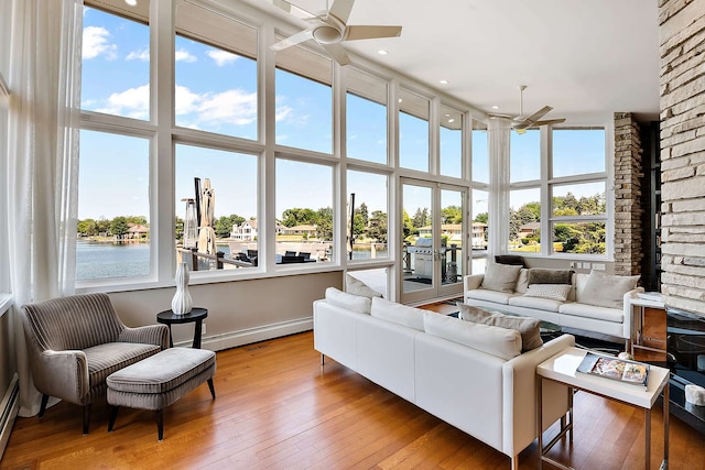 sunroom with ceiling fan, a water view, and a baseboard radiator