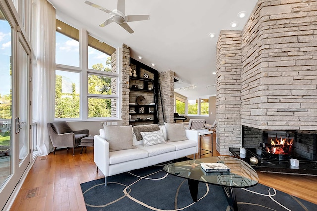 living room with wood-type flooring, a stone fireplace, ceiling fan, and a healthy amount of sunlight