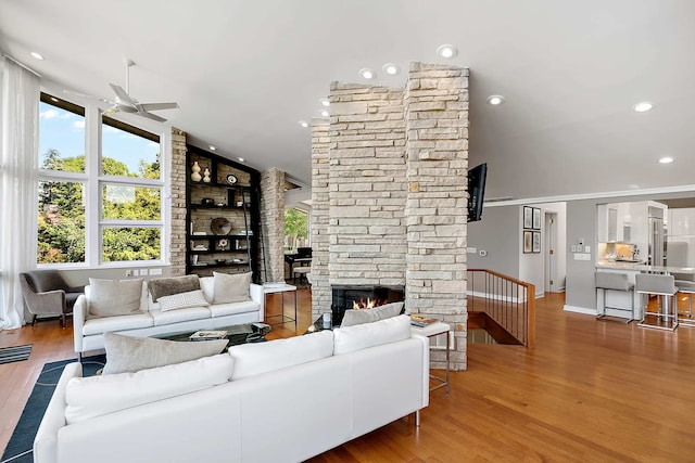 living room featuring a stone fireplace, ceiling fan, wood-type flooring, and vaulted ceiling