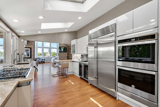 kitchen with appliances with stainless steel finishes, vaulted ceiling with skylight, sink, white cabinetry, and a breakfast bar area