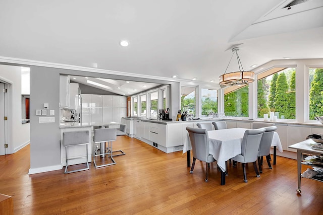 dining space with light wood-type flooring, vaulted ceiling, and an inviting chandelier