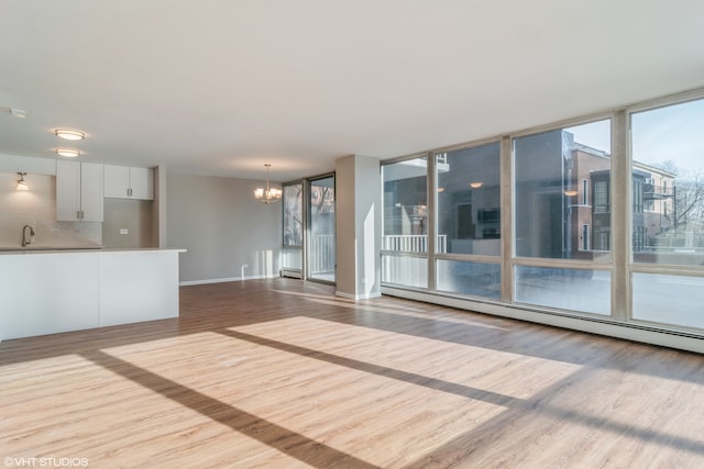 empty room with baseboard heating, sink, a chandelier, and light hardwood / wood-style floors